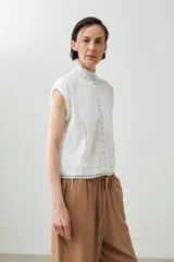 Blusa blanca sin mangas con cuello alto y detalles de puntilla.