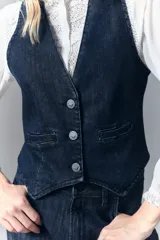Chaleco sastrero de denim azul oscuro con elastano, acceso con botones con logo, falsos bolsillos ojal y tira de ajuste en la espalda con hebilla. Bordado de alas en la espalda.