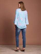 Blusa de seda fría estampada con flores en tonos celeste y rosa, marca Ruby Rd. Tiene cuello redondo con escote en V entrelazado y mangas 3/4 acampanadas.