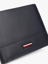 Billetera plegable de cuero negro con logo de Tommy Hilfiger esmaltado en el frente. Cuenta con compartimento para billetes y múltiples ranuras para tarjetas.