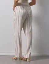 Pantalón de lino a rayas verticales color beige y blanco, con pretina ancha elastizada, lazo de ajuste y bolsillos inclinados.
