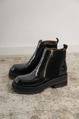 Botines negros de cuero con caña baja, puntera redondeada y cierre frontal con cremallera. Presentan paneles laterales de gamuza y suela track con plataforma.