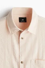 Camisa de manga corta color rosa claro, con cuello inglés, tapeta lisa, bolsillo superior abierto, canesú en la espalda y bajo recto.