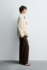 Blazer color beige confeccionado en tejido con lana, de corte relajado. Tiene cuello con solapas de muesca, manga larga con puños abotonados, bolsillo de vivo en el pecho, bolsillos de solapa en la cadera, bolsillo interior, bajo con abertura en el centro de la espalda y cierre frontal con botones.