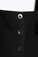 Chaleco negro con escote cuadrado, tirantes anchos y cierre frontal con tres botones.