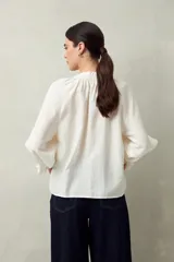Camisa color crema de lino con cuello redondo, canesú fruncido, mangas largas amplias con puños elastizados con volado y cierre frontal con botones.