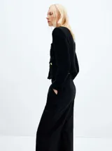 Chaqueta corta negra de tweed con botones dorados, cuello redondo y bolsillos frontales.