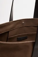 Bolso tipo shopper marrón de tejido de algodón con asas de cuero. Cuenta con dos bolsillos laterales exteriores y un bolsillo interno. Marca Mango.