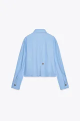 Camisa celeste de algodón con corte crop, cuello solapa, mangas largas con puños y cierre frontal con botones ocultos.