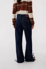 Pantalón de jean azul oscuro de corte recto, con cintura alta con cinturón del mismo material y detalle de flecos en la cintura y en los tobillos.