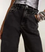 Pantalón de jean azul oscuro, corte barrel, con cintura con trabillas, cierre con botón y cremallera, bolsillos delanteros y traseros, y recortes en las rodillas y el bajo.