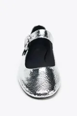 Zapato bailarina plateado con efecto metalizado, acabado en punta redonda y tira con cierre mediante hebilla metálica. Suela de 1,5 cm de altura.