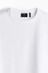 Remera blanca de corte holgado con cuello redondo ribeteado y hombros caídos. Confeccionada con tejido funcional COOLMAX®, una fibra de poliéster de secado rápido que elimina la humedad y regula la temperatura corporal.