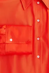 Vestido camisero largo color naranja, de corte amplio, con cuello clásico, cierre frontal con botones, mangas largas con puños abotonados, bolsillos laterales y tajos laterales pronunciados.