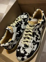 Zapatillas bajas con estampado animal print de vaca en blanco y negro, con cordones marrones y suela color caramelo.