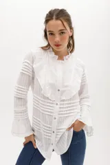 Camisa blanca de algodón con cuello mao y volados en el pecho, mangas largas con puños elásticos y cierre frontal con botones nacarados.