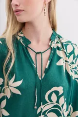 Camisa holgada verde esmeralda con estampado floral en color crema, escote redondo con abertura frontal y lazo de ajuste, mangas largas con puños elastizados con volados.