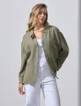 Camisa blanca de algodón con textura arrugada, cuello con solapa, abertura central con botones y bolsillo aplicado en el pecho. Mangas largas con largo regulable mediante presilla y botón.
