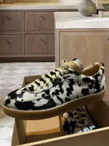 Zapatillas bajas con estampado animal print de vaca en blanco y negro, con cordones marrones y suela color caramelo.