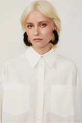 Camisa blanca amplia de algodón, con dos bolsillos en el frente, abotonada y con puños anchos.