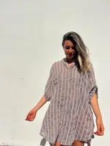 Camisero corto color habano con bordado de líneas verticales blancas. Tiene cuello camisero, mangas cortas y cierre frontal con botones.