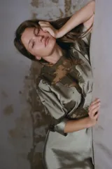 Vestido midi color verde oliva de tejido satinado, con cuello barco, mangas cortas abullonadas con puños y aplicación de encaje a contraste en la parte superior. Cierre trasero con cremallera oculta y botones forrados.