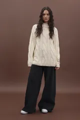 Sweater color crema de punto trenzado con cuello alto y mangas largas.