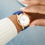 Reloj Guess modelo Mist con caja de acero en tono oro rosa de 35 mm y correa de silicona azul. Presenta una esfera plateada con indicadores y agujas en oro rosa, y un bisel con detalles de tornillos decorativos.