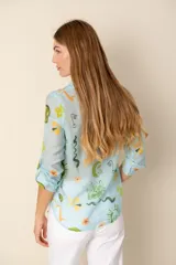 Camisa celeste con estampado de soles, lunas, flores y tortugas en tonos verdes, amarillos y naranjas.