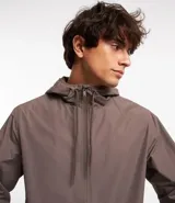 Campera rompevientos color verde oliva, con capucha ajustable con cordón, cierre frontal con cremallera, bolsillos laterales con cremallera y puños elásticos.