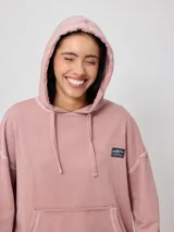 Canguro gris con capucha corta, bolsillo tipo canguro y parche con logo de la marca Rusty en el pecho. Tiene efecto lavado y costuras a la vista.