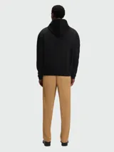 Buzo negro con capucha y cordones ajustables, corte holgado y pequeño logo bordado en el pecho. Se lleva sobre una camisa blanca de cuello.