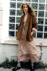 Vestido largo de gasa color rosa pálido con estampado floral en tonos dorados, escote en pico ajustable con lazada, mangas largas abullonadas con elástico y volantes en los puños, forro interior y bajo con volantes escalonados.