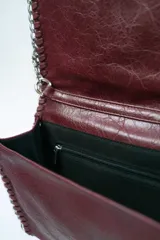 Cartera tipo sobre o clutch negra con textura de cuero envejecido. Presenta bordes decorados con costuras gruesas en contraste y una cadena metálica plateada que sirve como borde y correa de hombro.