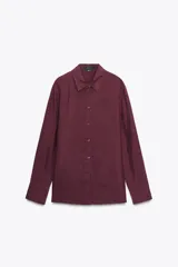 Camisa de manga larga color borgoña, confeccionada en seda 100%. Tiene cuello solapa, puños abotonados, bajo asimétrico redondeado y cierre frontal con botones.