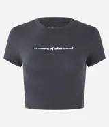Blusa corta gris oscuro, tipo baby tee, confeccionada en algodón, con cuello redondo y mangas cortas. Presenta un estampado frontal con la frase "in memory of when i cared".