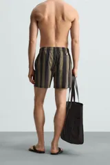 Bañador corto de tejido técnico con rayas verticales en tonos negro, verde oliva y rosa. Cuenta con cintura elástica ajustable con cordón, bolsillos laterales y trasero.