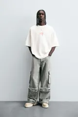 Pantalón relaxed fit de denim negro con efecto lavado, bolsillos frontales, traseros de plastrón y multifunción en perneras. Bajo ajustable con trabilla y cierre frontal con cremallera y botón.