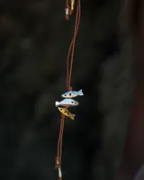 Gargantilla con hilo de algodón color camel y tres dijes de peces realizados en bronce, alpaca y plata 925.