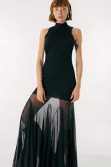 Vestido negro con cuello alto y corte ajustado hasta la rodilla. Falda larga de gasa transparente con diseño irregular. Sin mangas.