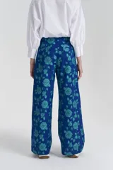 Pantalón de tiro alto con estampado de flores en tonos verdes sobre fondo azul, con bolsillos laterales.
