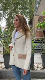 Campera color beige con cuello amplio y botones frontales, cuenta con bolsillos laterales de contraste.
