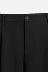 Pantalón negro de corte amplio, con pliegues en la parte delantera, bolsillos laterales y traseros de ojal.