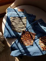Pantalón de jean azul con bolsillos traseros desmontables con estampado animal print. Los bolsillos se sujetan al pantalón con remaches metálicos.