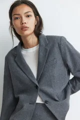 Blazer gris de corte entallado, con solapas de muesca, botonadura sencilla, bolsillo superior insertado y bolsillos delanteros. Tiene hombreras, botón decorativo en los puños y abertura atrás.
