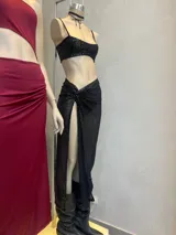 Conjunto de top y falda larga de lentejuelas negras. El top es tipo corpiño con tirantes finos y la falda tiene un corte irregular con abertura en la pierna y detalle de nudo en la cintura.
