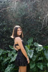 Vestido corto de lentejuelas color ciruela o morado oscuro, con escote corazón y detalle de argolla central que conecta con tirantes finos que atan al cuello. Presenta aberturas laterales (cut-outs) en la zona de la cintura y falda corta con vuelo.