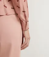 Camisa de viscosa color rosa con estampado de caballos en marrón. Tiene cuello camisero, cierre con botones, mangas largas, un bolsillo frontal y detalle de vivo contrastante.