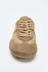 Zapatillas deportivas color beige con detalles en gamuza, estilo running, con suela dentada y ajuste con cordones.