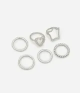 Set de seis anillos plateados de metal con diferentes diseños: tres anillos lisos, uno con forma de corazón con pequeñas bolitas, uno con forma de estrella y uno con pequeñas bolitas alrededor.